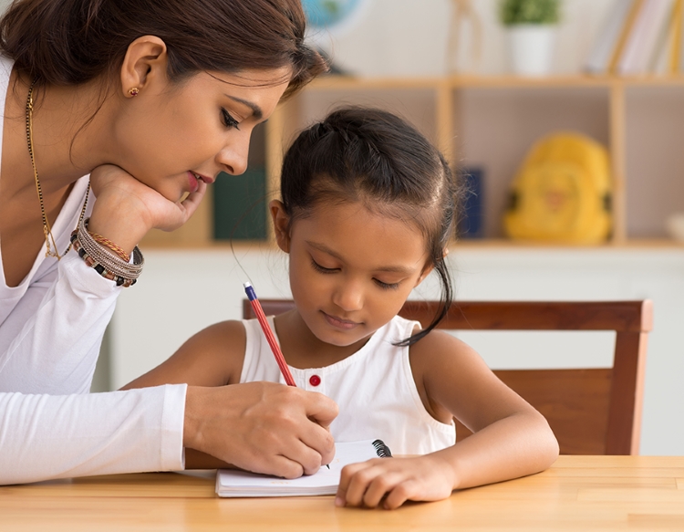 a mother watching over her daughter writing in a notebook